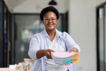 African American organizing documents in hand with colorful clips and sticky notes on desk,...