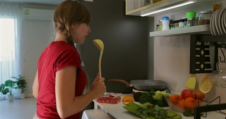 Woman cooking in kitchen, surrounded by fresh vegetables, modern interior, dancing, smiling, fun atmosphere, joyful cooking video for social media. - Powered by Adobe