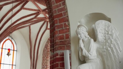 Praying angel statue is placed in a niche, beside a brick archway with a stained glass window - Powered by Adobe