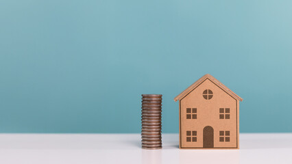 A house model placed next to a tall stack of coins, representing investment in property, home...