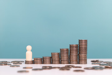 A wooden human figure stands next to a series of ascending stacks of coins, symbolizing personal financial growth, investment journey, and economic development over time