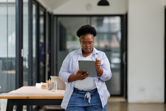 African American business woman using digital tablet while standing in workplace office. Black confident woman working on digital tablet in meeting room with copy space. Happy successful woman. - Powered by Adobe