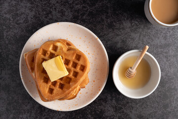 Heart shaped waffles with butter and honey on dark background