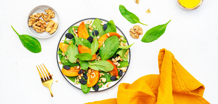 Yummy persimmon salad with walnuts, raisin and fresh spinach, white background, top view