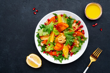 Delicious vegan salad with fresh persimmon, pomegranate seeds, walnuts, orange slices and lettuce