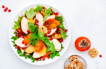 Yummy persimmon salad with grilled chicken, pomegranate, walnuts, oranges and lettuce, top view