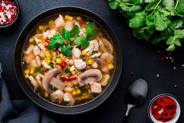 Mexican style chicken soup with mushrooms, corn, white beans, hot chili and cilantro. Black table background, top view