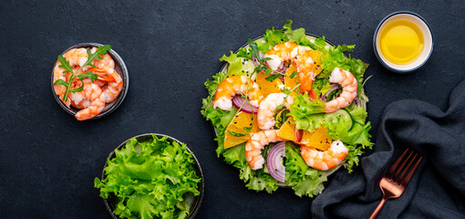 Juicy shrimp salad with orange, lettuce, red onion with olive oil and juice dressing, black background, top view