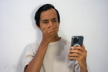 Shocked man looking at phone, hand over mouth.