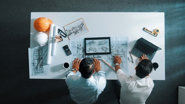 Top view of skilled civil engineer working together to plan building design while using laptop. Professional architect team sitting at table while manager using tablet open project plan. Alimentation.