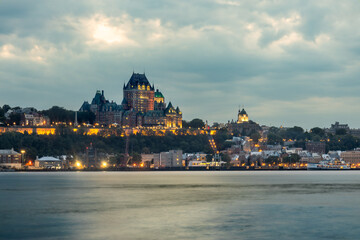 Fototapeta premium Distant view of Château Frontenac in Quebec City during sunset, with the St. Lawrence River in the foreground and warm light bathing the historic landmark.