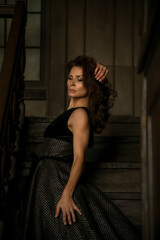 A woman rests her chin on her hand while sitting on a staircase. The warm lighting highlights her features and the vintage decor surrounding her, creating an intimate atmosphere.