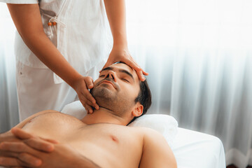 Obraz premium Caucasian man enjoying relaxing anti-stress head massage and pampering facial beauty skin recreation leisure in dayspa modern light ambient at luxury resort or hotel spa salon. Quiescent