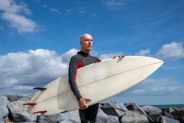 Surfer in wetsuit carrying surfboard on a rocky beach