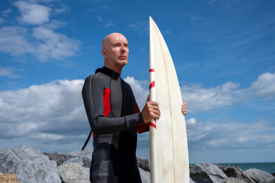 surfer standing on a beach holding a surfboard wearing a wetsuit