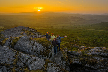 Obraz premium Family hiking on Dartmoor tors at sunset, silhouetted against dramatic skies in scenic moorland landscape