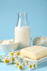 Fresh dairy products and chamomile flowers on light blue background, closeup