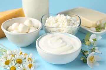 Fresh dairy products and flowers on light blue background, closeup