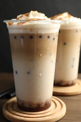 Tasty milk bubble tea in plastic cups on wooden table, closeup