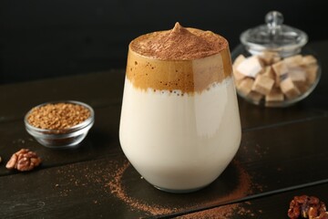 Delicious dalgona coffee in glass, granules, walnuts and brown sugar on wooden table, closeup