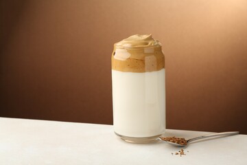 Delicious dalgona coffee in glass and granules on white table, space for text