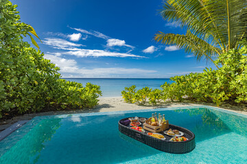 Luxurious floating breakfast tray in infinity pool at tropical luxury resort. Vacation sea view palm leaves closeup of food and drinks in morning sunlight, perfect for exotic summer holiday background