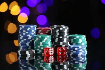 Casino chips and dice on mirror surface against blurred lights, closeup