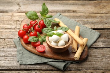 Tasty mozzarella cheese balls, tomatoes, basil and grissini on wooden table
