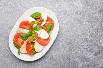 Tasty salad Caprese with mozzarella, tomatoes, basil and pesto sauce on grey table, top view. Space for text