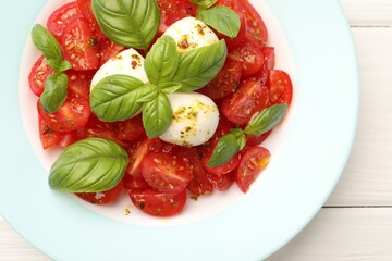 Tasty salad Caprese with mozzarella, tomatoes, basil and spices on white wooden table, top view