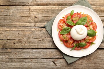 Tasty salad Caprese with mozzarella, tomatoes, basil and pesto sauce on wooden table, top view. Space for text