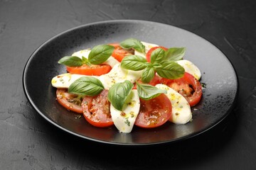 Tasty salad Caprese with mozzarella, tomatoes, basil and spices on black table, closeup