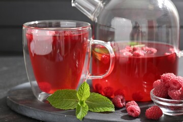 Aromatic raspberry tea in glass cup, teapot, berries and mint on table, closeup