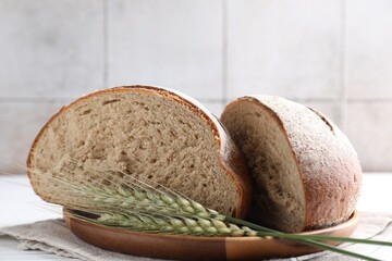 Pieces of fresh bread and green spikes on white table, closeup