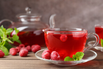 Tasty raspberry tea in glass cup, teapot, berries and mint on wooden table, closeup