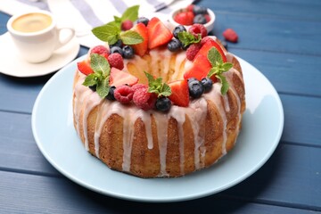 Delicious bundt cake with berries, glaze and mint on blue wooden table, closeup