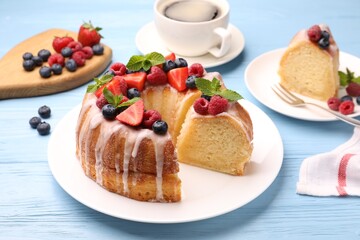 Pieces of delicious bundt cake with berries, glaze and mint on light blue wooden table, closeup