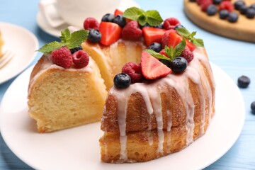 Pieces of delicious bundt cake with berries, glaze and mint on light blue wooden table, closeup