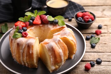 Pieces of delicious bundt cake with berries, glaze and mint on wooden table, closeup