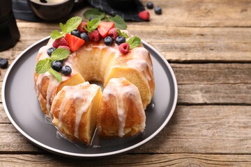 Pieces of delicious bundt cake with berries, glaze and mint on wooden table, closeup