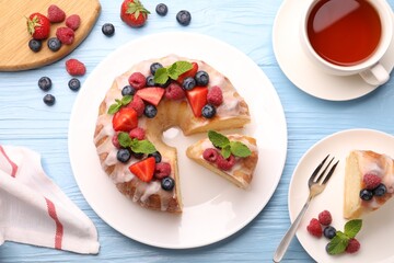 Pieces of delicious bundt cake with berries, glaze and mint served on light blue wooden table, flat lay