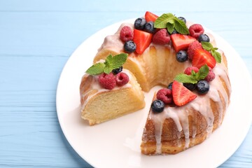 Pieces of delicious bundt cake with berries, glaze and mint on light blue wooden table, closeup