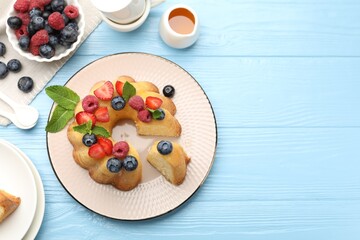 Tasty Bundt cake with berries, honey and mint on light blue wooden table, flat lay. Space for text