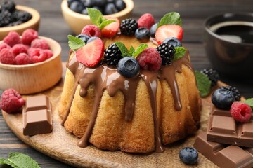 Tasty Bundt cake with berries, chocolate, mint and coffee on wooden table, closeup