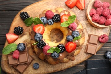Tasty Bundt cake with berries, chocolate and mint on wooden table, top view
