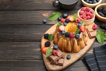 Tasty Bundt cake with berries, chocolate, mint and coffee on wooden table, above view. Space for text