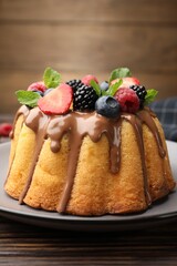 Tasty Bundt cake with berries, chocolate and mint on wooden table, closeup