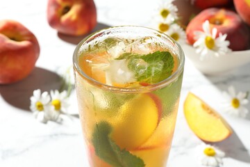 Tasty iced peach tea in glass, fresh fruits, mint and chamomile flowers on white table, closeup