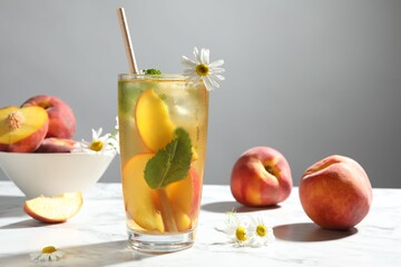 Tasty iced peach tea in glass, fresh fruits, mint and chamomile flowers on white table