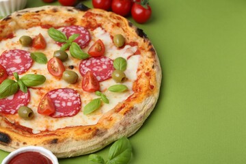 Delicious pizza with salami, olives, tomatoes and basil on green table, closeup. Space for text
